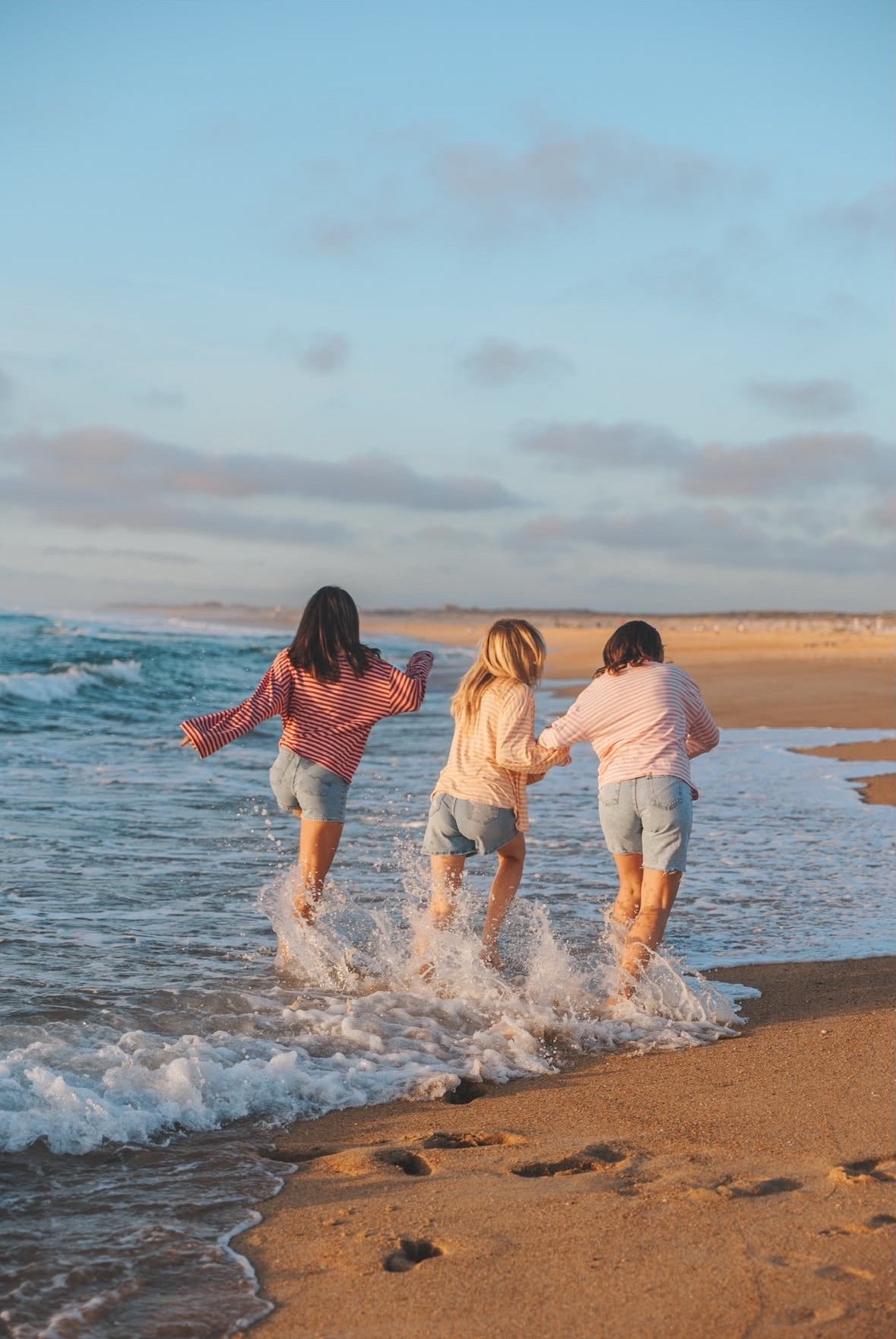 Trois amies qui courent dans les vagues au coucher du soleil